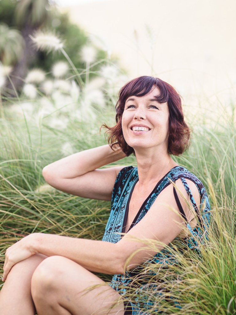 smiling woman sitting in grasses at Leisure Island during personal branding session photographed by moira du toit of moi du toi photography