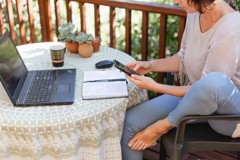 woman sitting with computer and coffee cup on outdoor wooden deck in garden at Knysna during personal branding session photographed by moira du toit of moi du toi photography