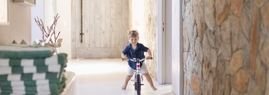 little boy riding his bike down hallway during light and airy slice of life family session at Cola Beach by sedgefield photographer moi du toi