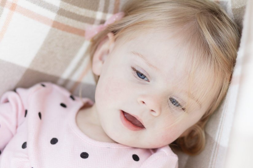 Close up head and shoulders of a little girl with blue eyes and blonde hair lying on a check blanket during a lifestyle family photo shoot by a Sedgefield photographer moi du toi photography