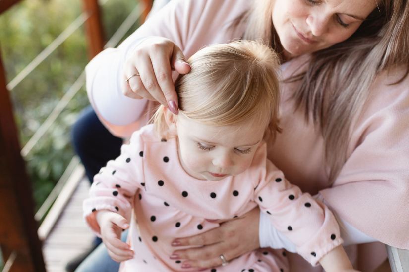 Mom wearing pink and stroking hair on baby daughter's head during a lifestyle family photo shoot by a Sedgefield photographer moi du toi photography