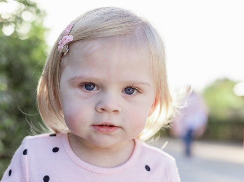 Close up backlit head and shoulders of a little girl with blue eyes and blonde hair during a family lifestyle shoot with photographer moi du toi photography