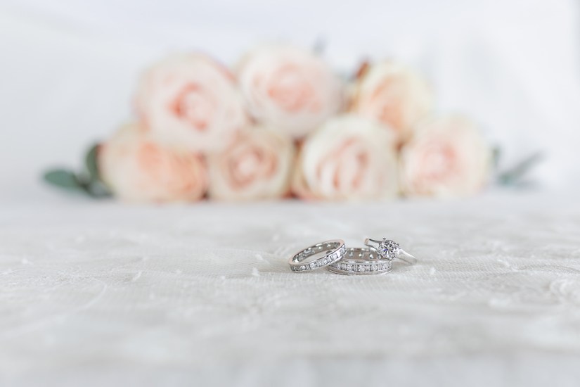 2 wedding rings and engagement ring with roses in the background