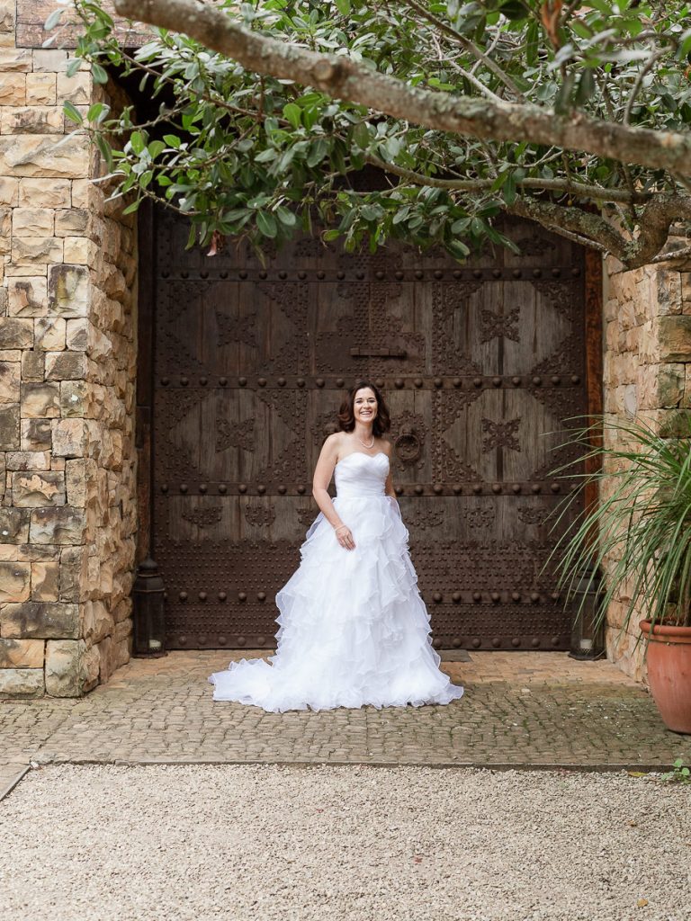Dark haired gay bride in a off the shoulder white dress posing in front of wooden doors at luxury wedding venue sedgefield
