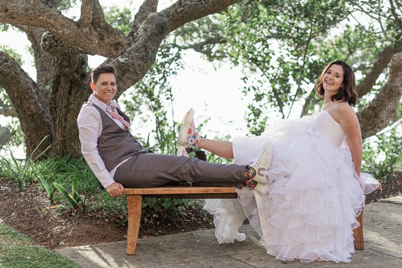 gay wedding couple sitting on garden bench showing off their high top gay pride sneakers
