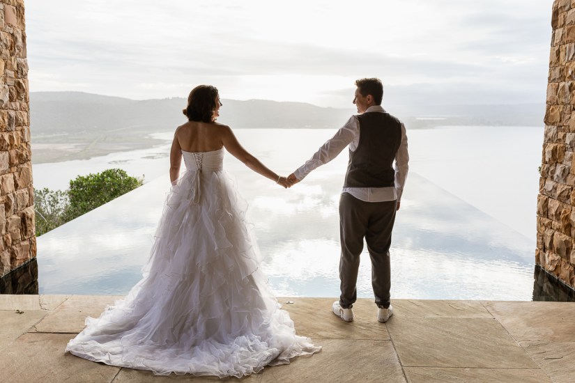 Gay coiuple holding hand and standing in front of an infinity pool at luxury wedding venue Cloud 9 sedgefield